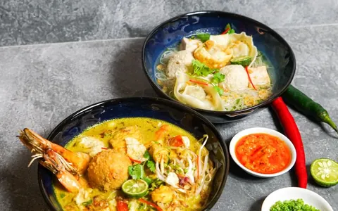 Bowls of seafood laksa with noodles and garnishes