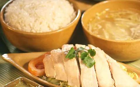 Slices of poached white chicken beside rice, soup and sauces